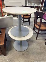 Front view of one round side table showing white top, gray base with tiered circular platforms.