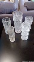 Five clear glass vases with varying patterns and heights on a black table