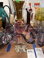 Four glass vases displayed on table, showing diverse styles including clear purple ruffled vase, tall purple vase, tortoiseshell patterned Maestri Vetrati vase, and teal green vase.