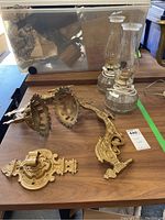 Overview of two clear glass electric lamps with vintage oil lamp style and three ornate metal wall sconce mounts on wood surface