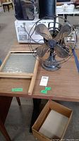 Photo shows vintage GE fan with five metal blades in protective wire cage beside wood framed glass washboard on table.