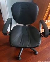 Front-facing photo of a black leather office chair with armrests and caster wheels, showing condition and design.