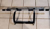 Door pull-up bar laid flat on tiled floor showing the metal frame and black foam padded grips and support.
