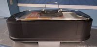 Photo showing a rectangular portable electric grill with a black base and transparent glass lid with handle.