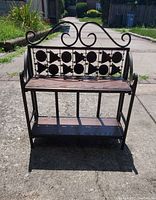 Front view of the iron collapsible two-tier shelving unit showing decorative scroll and leaf pattern and wooden slat shelves.