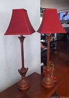 Pair of metal table lamps with bronze bases and red shades, shown side by side on a table.