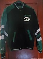 Green and black suede New York Jets varsity jacket with logos and striped sleeves.