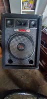 Front view of Gen Sound party speaker showing woofer behind metal grille, two horn tweeters, brand label, and bass ports.