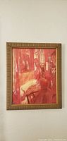Framed abstract painting with warm red and pink tones, displayed on a white wall.