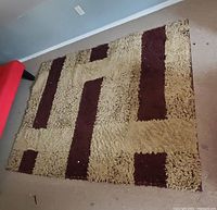 Rug with a geometric design featuring beige and dark brown colors, photographed laid flat on carpeted floor.