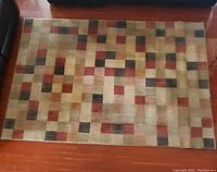 Rectangular multicolor geometric pattern rug on hardwood floor between furniture, showing overall pattern and condition.