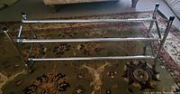 Photo of a metal shoe rack with tubular frame and multiple horizontal rods on carpeted floor