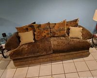 Brown fabric sofa with multiple cushions and rounded armrests on tiled floor under a lamp.