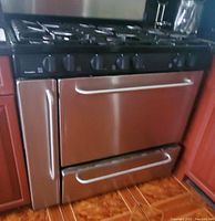 Front view of stainless steel gas range showing cooktop with 6 burners, control knobs, oven door, and storage drawer