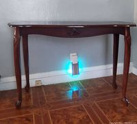 Front view of a wood console table with decorative carvings and claw feet on tiled floor.