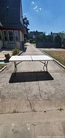 Full view of the folding table set up outside on a driveway, showcasing the entire table length and supporting legs.