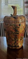 Front view of ceramic vase with lid and upward curved handle. Shows detailed floral and abstract design.