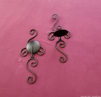 Two metal wall candle holders with scroll detail on a red background.