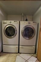 Front view of white Whirlpool Duet washer and dryer set side-by-side on pedestals in alcove.