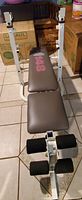 Full view of weight bench showing padded backrest and seat with leg curl attachment and foam rollers.