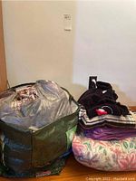 Green cloth bag filled with various linens and towels, placed next to folded blankets and children's robe