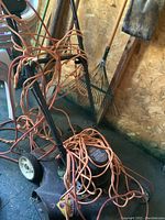 Electric lawn mower with attached orange extension cord and reverse style handle, showing general condition and size.