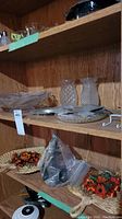 Shelf with various glassware including textured vases and dishes, wall fans with fabric flowers, and pins in packages