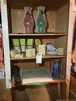Wooden shelf contains two Christmas hurricane candles wrapped in white mesh, several yellow and black Powerhouse appliance modules in original packaging, antique hand plane and two square tiles.