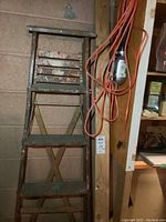 Vintage wooden ladder with four wide steps showing paint wear and age, standing against a wall.
