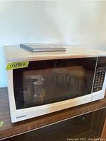 White Danby microwave oven with black glass front and keypad visible, measuring approximately 21x15x11 inches.