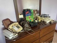 Photo showing 3 phones, brown pleather camera bag, boxed Zellers headphone radio, and other assorted electronics on a dresser