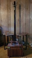 Wood coat rack, two demi-lune tables, and shoeshine box in room with wood panel walls and brown carpet