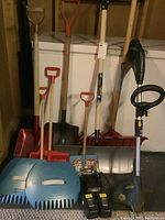 Wide view showing all shovels, leaf grabbers, and Yardworks battery trimmer with accessories in one frame.