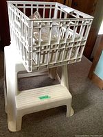White resin molded step stool with a white plastic crate on top, seen from front angle