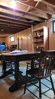 Full view of vintage solid wood dining table with three matching wooden spindle back chairs set in basement room, visible water damage on table surface