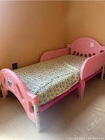 Full view of the pink plastic toddler bed with patterned fabric mattress cover, showing headboard and side rails.
