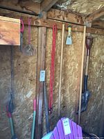 Wooden wall with hanging garden tools including spade, fork, clippers, and bungee cord