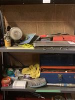 Photo showing metal tool box with hand tools and socket wrench set, soldering kit, flood light, and assorted cleaning tools on shelf.