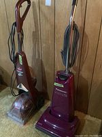 Two floor cleaning appliances standing side by side: Panasonic platinum upright vacuum and Bissell Quick Steamer carpet cleaner against wood panel wall.