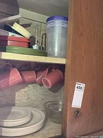 Cabinet shelf showing stacked white plates, clear Pyrex bowl, and pink ceramic mugs hanging from hooks