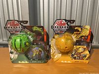 Front view of two Bakugan Evolutions toys in original packaging, Turbo Wynton (green) and Turbo Dragonoid (yellow).