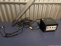 Nintendo GameCube console and AV cable viewed from an angle on a blue surface.