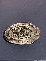 Front view of the oval metal belt buckle showing detailed embossed Jack Daniel's whiskey branding and logo.