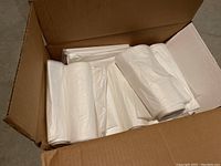 Open cardboard box showing multiple white garbage bags rolled and stacked inside.