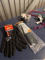 Photo shows black Ninja brand gloves, a roll of silver duct tape, and package of black zip ties on a blue table.