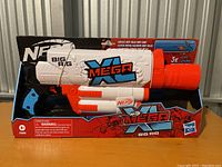 Front view of Nerf Mega XL Big Rig blaster in packaging showing front side with branding and included darts.