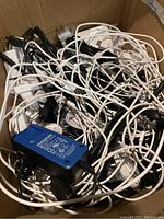 Top-down view of a box full of tangled white and black power cables with visible power adapters including one blue Telebyte power adapter.