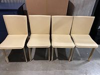 Front view of four beige leather dining chairs lined up, showing seat and backs.