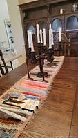 Long view of wooden five-candle holder with white taper candles, two single wooden candlestick holders, boxed candles, and table runner on wooden dining table.