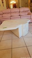 Photo of the white coffee table showing overall shape and color in front of pink sofa, placed on tiled floor.